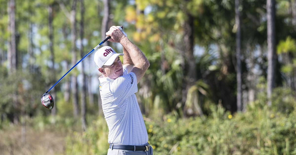 Jim Furyk swinging a driver on the course with trees in the background.