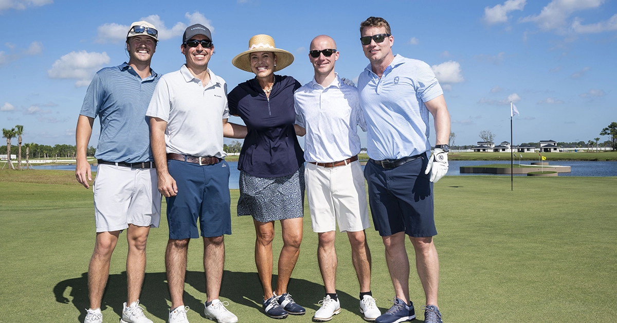 Group of golfers posing together on the green with water behind them.