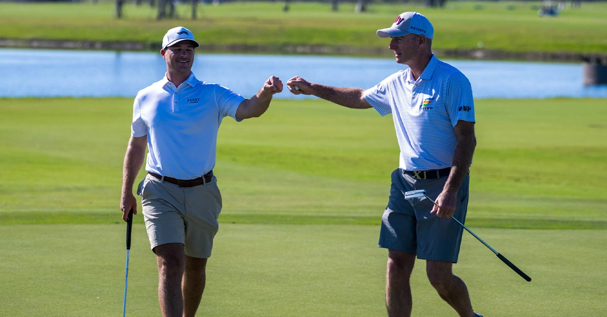 Two golfers giving a fist bump on a putting green.