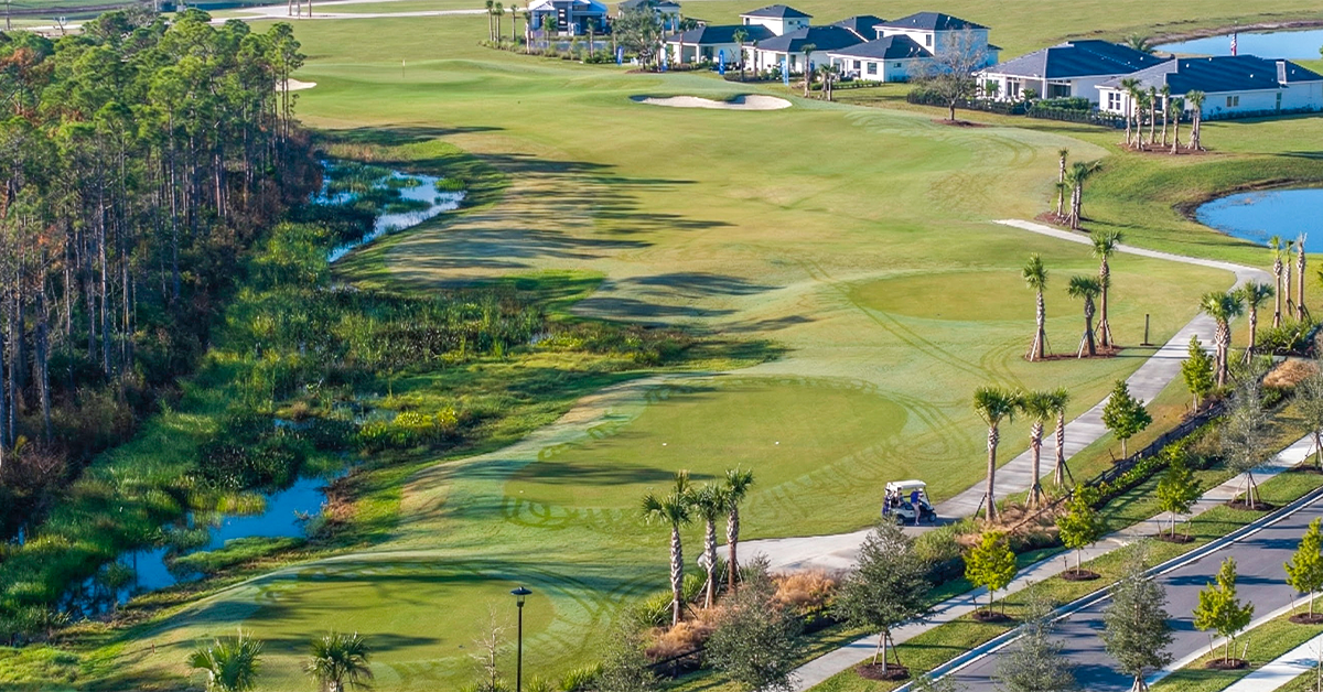 Wide aerial view of golf fairway bordered by wetlands and homes