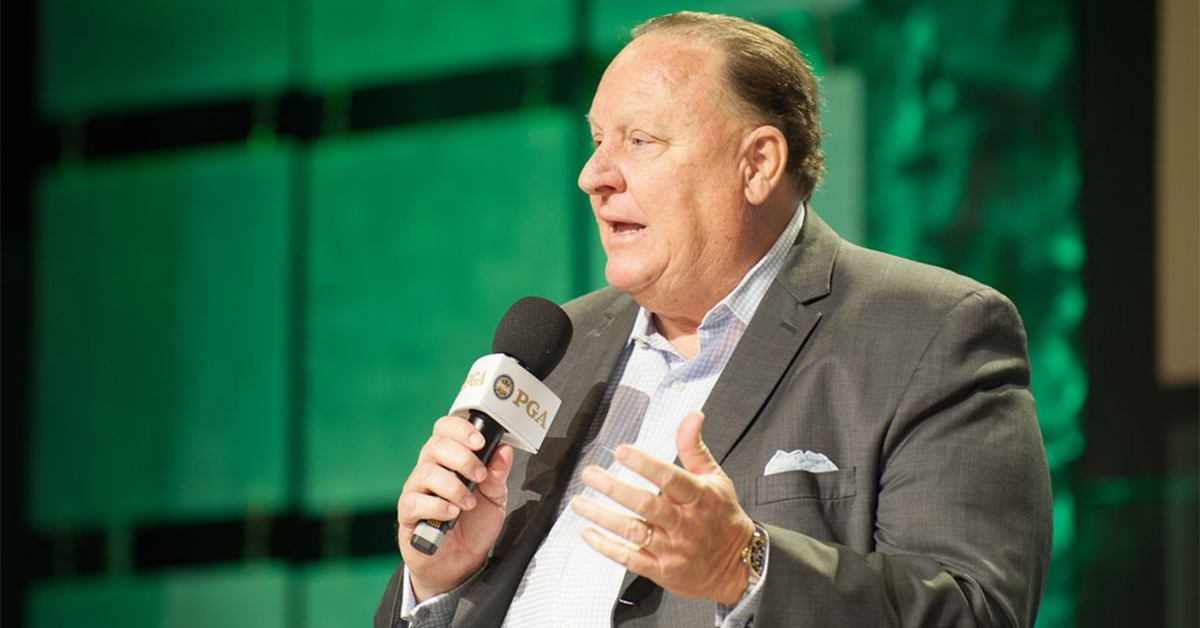 M.G. Orender speaking into a handheld microphone on stage