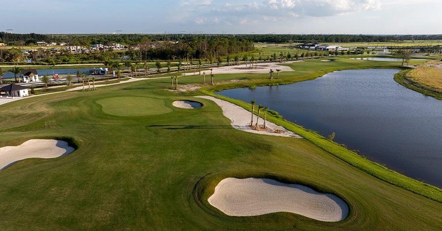 Golf fairway with sand bunkers beside a water hazard under blue sky.