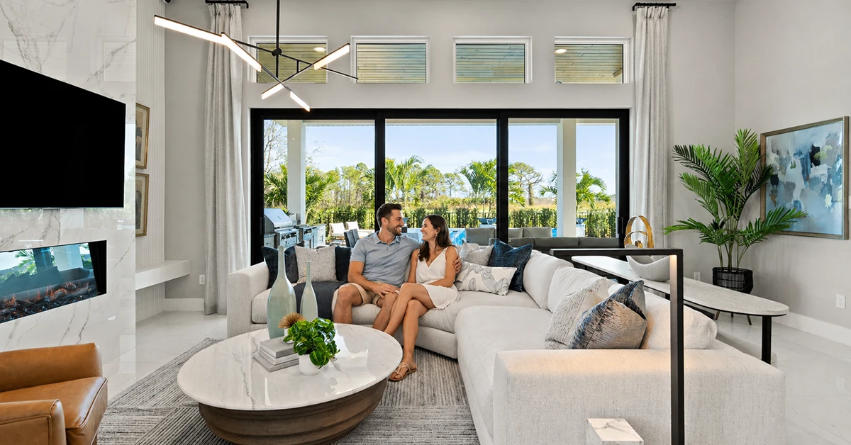 Couple sitting on sofa in modern living room with large glass doors and outdoor view