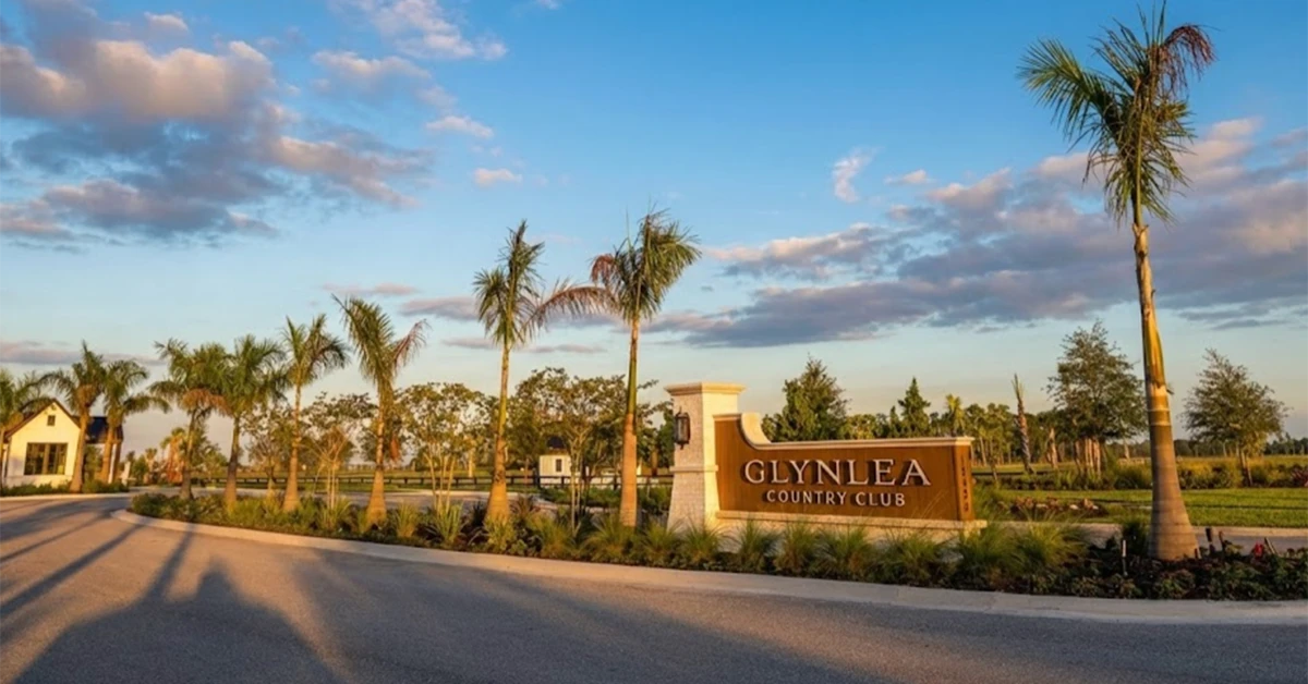 Entrance sign for Glynlea Country Club with palm trees and landscaped road under blue sky