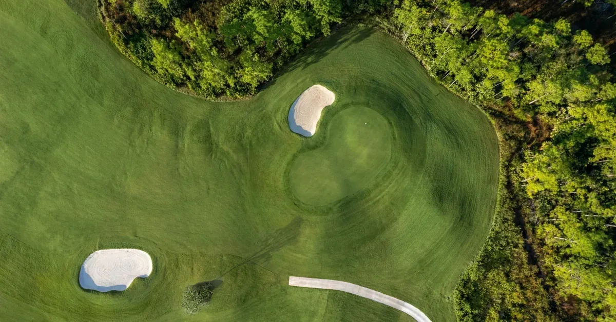 Aerial view of a pristine golf course green surrounded by sand bunkers and lush forest, showcasing resort-style amenities.