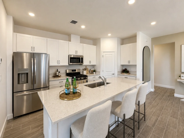 Kitchen with white cabinets, stainless steel refrigerator and range, and a large quartz island with three barstools.