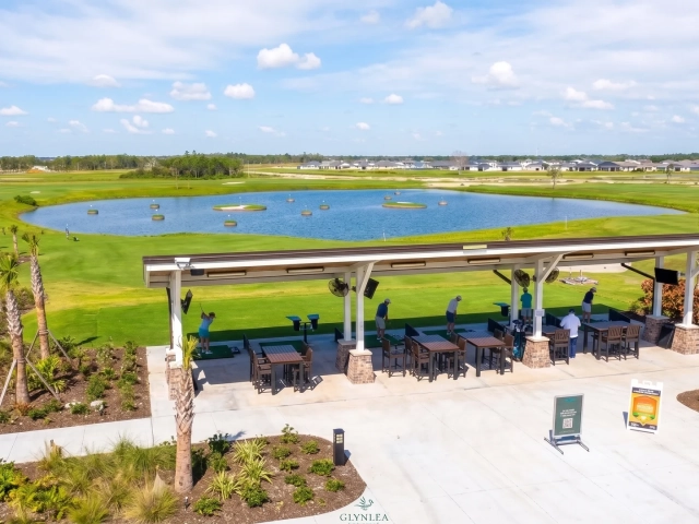 Elevated view of a covered driving range bay structure labeled Glynlea, overlooking a pond with floating golf targets.