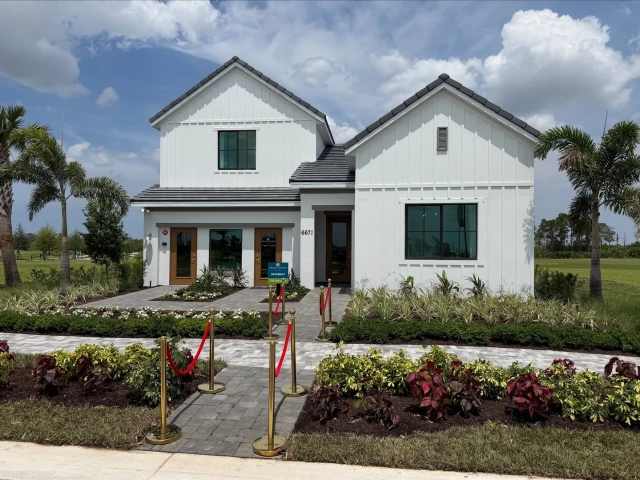 Two-story white model home with a Ravenna II sign and gold stanchions with red rope lining the front walkway.