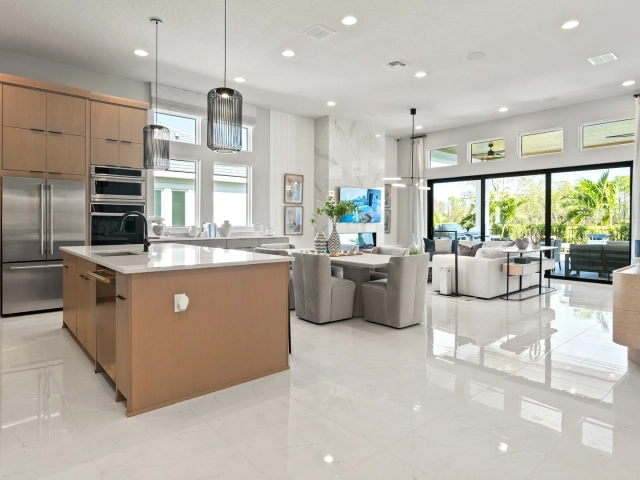 Kitchen with light wood cabinets, a large island, black pendant lights, and an open great room with glossy tile flooring.
