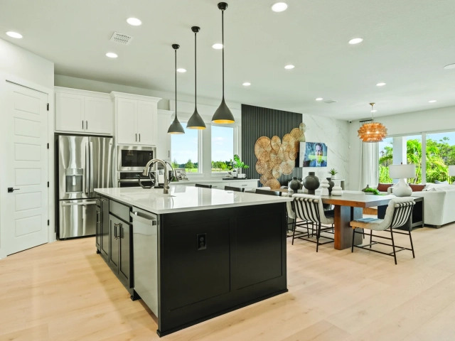 Kitchen with white cabinets, a black island, three black cone pendant lights, and an open dining and living room beyond.