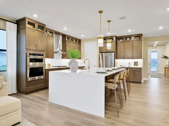 Kitchen with dark wood cabinets, stainless steel double ovens and refrigerator, and a large white quartz island with bar seating.
