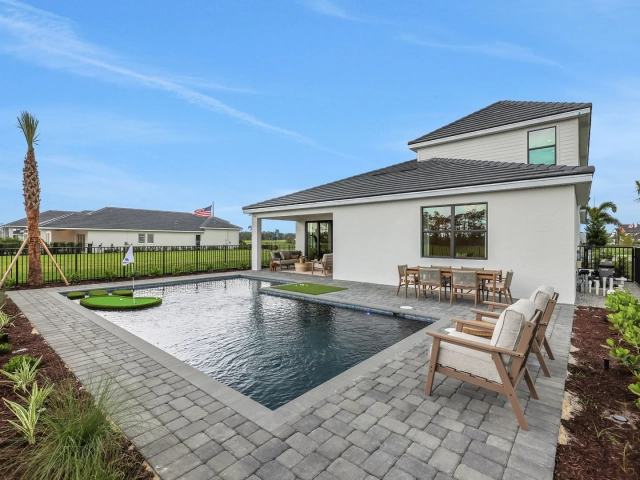 Backyard pool with attached putting green, covered patio with outdoor dining table, and lounge chairs beside the pool.